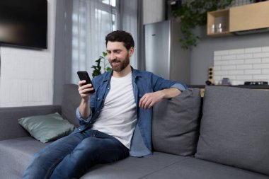 Mutlu adam gülümsüyor ve evdeki koltukta oturuyor.