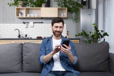 Mutlu adam gülümsüyor ve evdeki koltukta oturuyor.