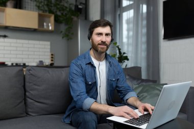 Evden uzak bir çağrı merkezi operatörü olarak çalışan bir adamın portresi. Koltukta otururken kulaklık ve dizüstü bilgisayar kullanıyor.