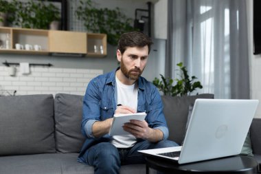 Erkek serbest çalışan uzaktan eğitim veriyor, dizüstü bilgisayar kullanıyor, webcam 'e bakıyor, öğrencilere ekonomik teoriyi anlatıyor.