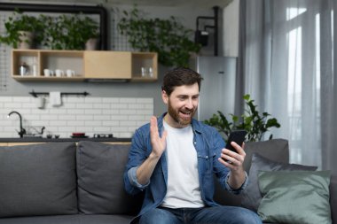 Evdeki adamlar telefonda video görüşmesi yapıyorlar. Başvuruyu iletişim kurmak için kullanıyorlar. Kanepede oturup kameraya el sallıyorlar.