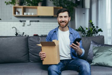 Evdeki adam çevrimiçi dükkandan bir sipariş aldı, Happy karton bir kutuyu paketle açtı, telefonuyla olumlu bir yanıt bıraktı.