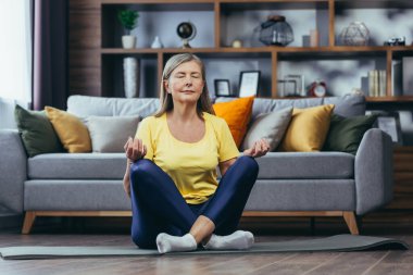 Yaşlı beyaz saçlı kadın evde yalnız, aktif yaşam tarzı, yoga, nilüfer pozisyonu ve meditasyon