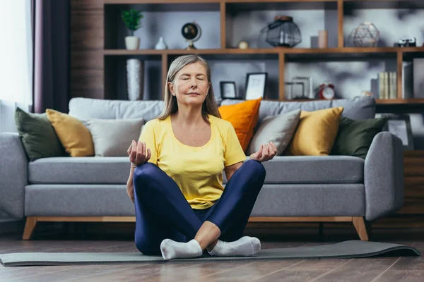 Yaşlı beyaz saçlı kadın evde yalnız, aktif yaşam tarzı, yoga, nilüfer pozisyonu ve meditasyon