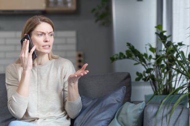 Evdeki sinirli kadın kanepede oturuyor ve telefonda konuşuyor.