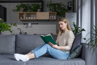 İşten sonra evde dinlenen güzel bir kadın, kanepede oturmuş ilginç bir kitap okuyor.