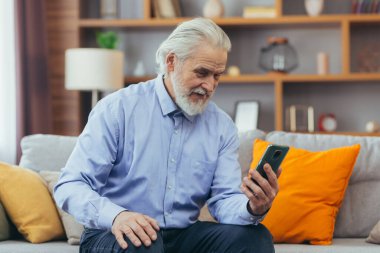 Evdeki son sınıf öğrencisi kanepede oturmuş telefon ekranına bakıyor, ailesiyle görüntülü konuşuyor.