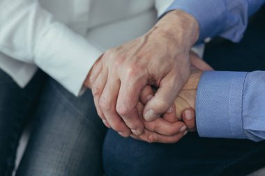 Yaşlı insanların ellerini kapayın. Yaşlı adam evde birlikte oturan bir kadının elini tutuyor. Yaşlı çift olgun aile koca ve büyük anne ve büyük baba birlikte evliliğe olan güveni destekliyor. Yakın çekim.