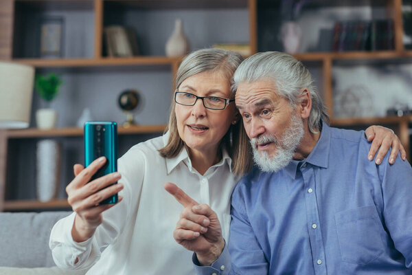 Elderly couple of senior retirees Happy gray haired grandparents communicate online in a video call using a mobile phone smartphone. laugh and wave hands. mature couple Remote meeting with children