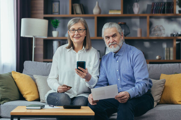 senior family couple, gray haired older pay, services enter data documents using application mobile smartphone credit card. Retirees elderly at home. utility bills, checks use computer smart phone