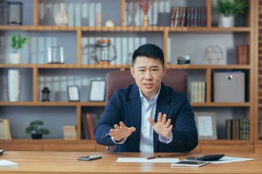 Ciddi ve kızgın işadamı, iş arkadaşlarıyla konuşurken kameraya bakıyor.