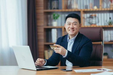 Genç ve başarılı bir Asyalı bankacı, elinde kredi kartı olan bir bankacı, bir video görüşmesinde dizüstü bilgisayarla konuşan, danışmanlık yapan, satan. Kameraya bakıyor, gülümsüyor.