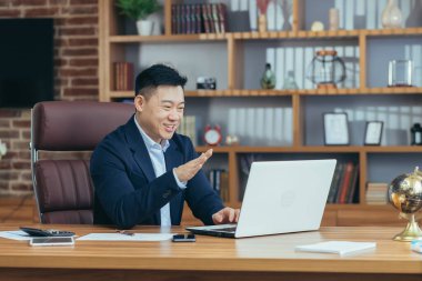 Yakışıklı Asyalı genç bir adam, iş adamı, avukat, yönetmen ofisteki bir bilgisayardan video görüşmesi yapıyor, toplantı yapıyor, danışmanlık yapıyor, tartışıyorlar.