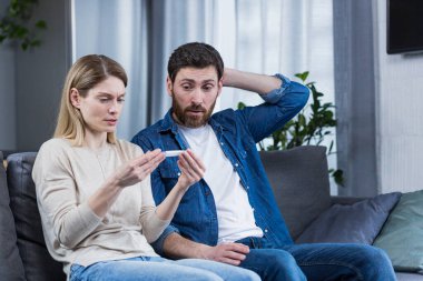 Üzgün adam ve kadın kanepede oturuyor, negatif hamilelik testi yüzünden hayal kırıklığına uğramışlar.