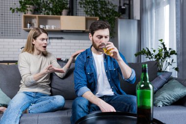 Alkolik bir koca evde karısıyla tartışıyor, kanepede oturuyor.