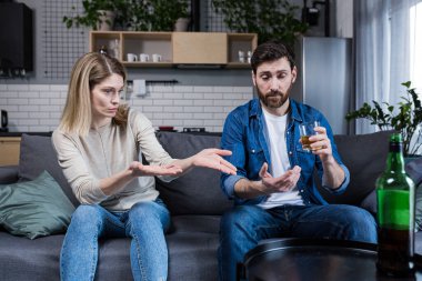 Alkolik bir koca evde karısıyla tartışıyor, kanepede oturuyor.