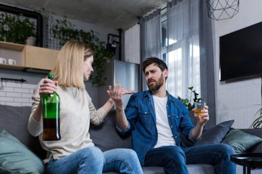 Alkolik bir koca evde karısıyla tartışıyor, kanepede oturuyor.