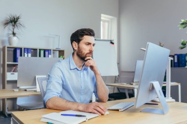 Odaklanmış tasarımcı modern bir stüdyoda çalışıyor. Adam gündüzleri bilgisayar başında çalışıyor.