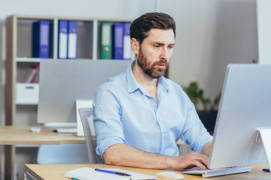 Odaklanmış tasarımcı modern bir stüdyoda çalışıyor. Adam gündüzleri bilgisayar başında çalışıyor.