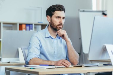 Odaklanmış tasarımcı modern bir stüdyoda çalışıyor. Adam gündüzleri bilgisayar başında çalışıyor.