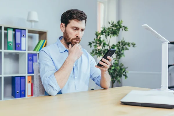 Upset and sad businessman looking at phone screen, man working in bright office