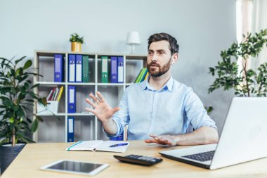 Ofiste çalışan bir adam telefonda konuşuyor. Küçük beyaz bir kulaklık kullanıyor. İş adamı.