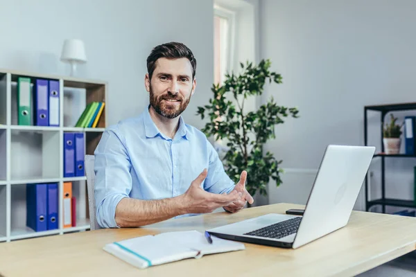 İş adamı dizüstü bilgisayarda konuşuyor, video kamera, iş yerindeki adam, kameraya bakıyor ve gülümsüyor, başarılı bir çalışan.