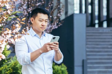 Ciddi ve düşünceli Asyalı işadamı telefonda yazıyor, ofisin dışında bir adam.