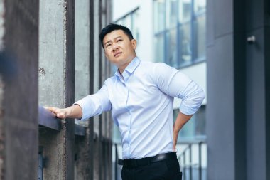 Ofis yakınlarında yorgun Asyalı iş adamı sırt masajı yapıyor, sırt ağrısı var, patron mola verdi.