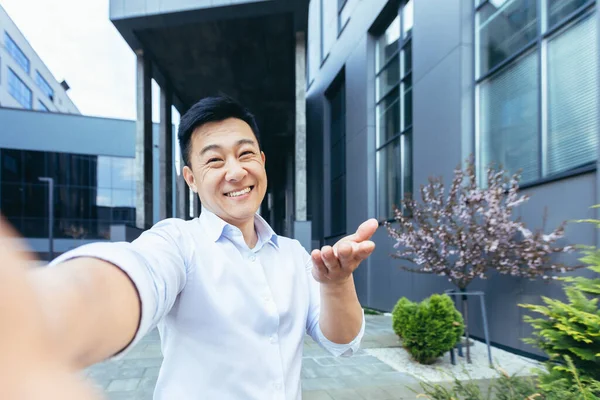 Videodaki Asyalı konuşması telefonu kullanıyor, kameraya bakıyor ve el sallayarak selamlama hareketi yapıyor.