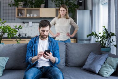 Conflict, young couple, family, man and woman. An angry woman shouts at a man who constantly uses and plays on the phone, does not pay attention
