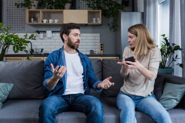 Conflict, quarrel, jealousy in the family home. Young couple, man and woman. The woman is jealous, takes the phone from her husband, demands an explanation