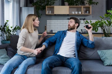 Conflict, quarrel, jealousy in the family home. Young couple, man and woman. The woman is jealous, takes the phone from her husband, demands an explanation