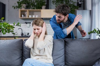 Aile içi şiddet. Aile çatışması. Bir adam evde bir kadına bağırıyor. Kadın kulaklarını kapattı. Kanepede oturuyorum..