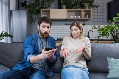 Family conflict at home. An angry man suspects a woman of treason, shouts at her, demands explanations, shows the phone, messages.
