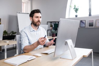 Freelancer bilgisayar ekranına bakıyor, görüntülü konuşan bir adam, ofiste uzaktan çalışan bir iş adamı.