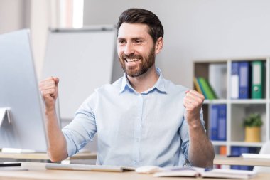 Başarılı serbest yazar bilgisayar ekranına bakar, sevinir ve başarıyı kutlar. Zafer için el kaldırır.