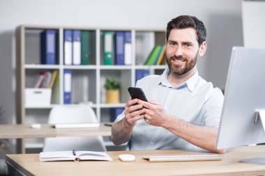 Ofisteki bilgisayar masasında cep telefonu kullanarak oturan mutlu, yakışıklı bir ofis çalışanı. Neşeli sakallı iş adamı girişimci işçi. Akıllı telefonları tarar, mesajları okur, iletişim kurar.