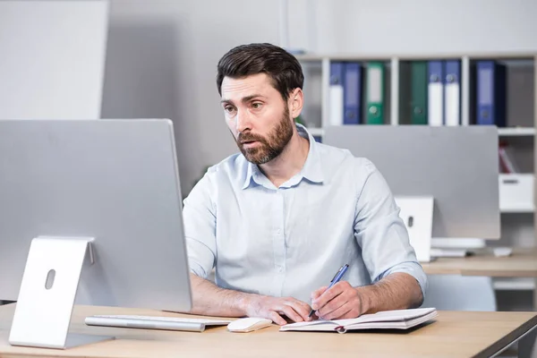 Concentrated and pensive businessman working in the office at the computer, paperwork broker, man looking at the monitor