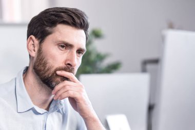 Portrait. Close up photo. Tired and thoughtful office worker. Sitting at a desk in the office, at the computer, holding his head in his hands, tired, in a white shirt