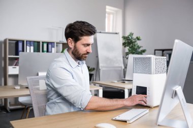 Genç yakışıklı bir adam, ofis çalışanı, çalışma odasındaki bilgisayarın yanında duran nemlendirici, klima ve klima dahil.