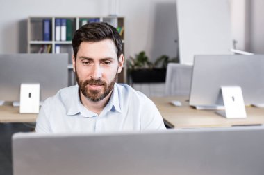 Genç bir adam, bir ofis çalışanı bilgisayarın ofisindeki bir masada oturuyor, bilgisayar kamerasıyla video görüşmesi yapıyor, ortaklarla, müşterilerle iş görüşmesi yapıyor..