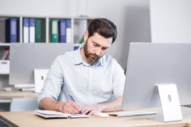 Bilgisayarında ve defterinde yazı olan orta yaşlı yakışıklı bir adam.