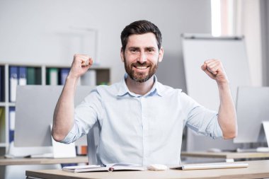 Genç, başarılı bir adamın portresi, ofis çalışanı, yönetici, serbest çalışan yapılan işin sonucuna sevinir. Masada ve bilgisayarda mutlu oturuyor, seviniyor, ellerini kaldırıyor, kameraya bakıyor, gülümsüyor.