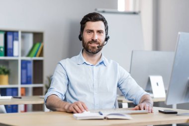 Video görüşmesi için kulaklığı olan bir adamın portresi. Ofiste çalışan ve gülümseyen bir adam.
