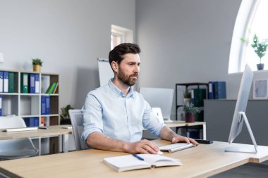 Bilgisayarın ofisinde çalışan ciddi bir iş adamı monitöre dikkatle bakar.