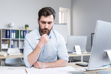 Genç bir mimar, tasarımcı, çizimler yapıyor ve ofisteki masanın üstündeki kağıt üzerinde proje yapıyor. Bilgisayarla bir masada oturup, odaklanmak...