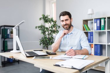 Ofiste çalışma ortamı. Genç bir iş adamının portresi, ekonomist, büroda çalışan bir yönetici, bir dizüstü bilgisayar, kağıtlarla çalışıyor. Belgeler.