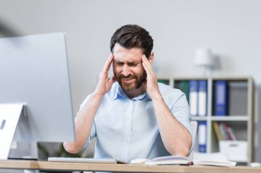 Yorgun ve sinirli genç bir adam, ofis çalışanı, başını tutan bir yönetici, ağrı, baş dönmesi. Ofisteki bir bilgisayar masasında oturmak..