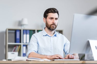 Genç bir adamın portresi, odaklanmış ve ciddi bir ofis çalışanı, yönetici, bilgisayar başında çalışan, ofiste bir masanın arkasında oturan